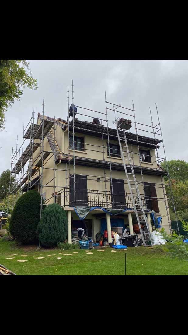Des échafaudages sur la façade d'une maison et un homme sur le toit