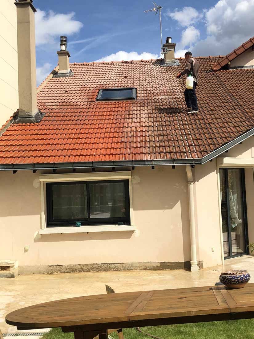 Un homme applique un produit de protection sur un toit en tuiles