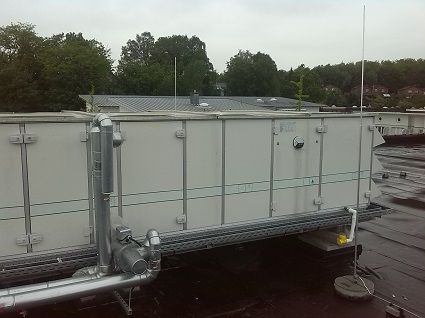 Große, weiße Industrie-Klimaanlage auf einem Flachdach mit außenliegenden silbernen Rohrleitungen.