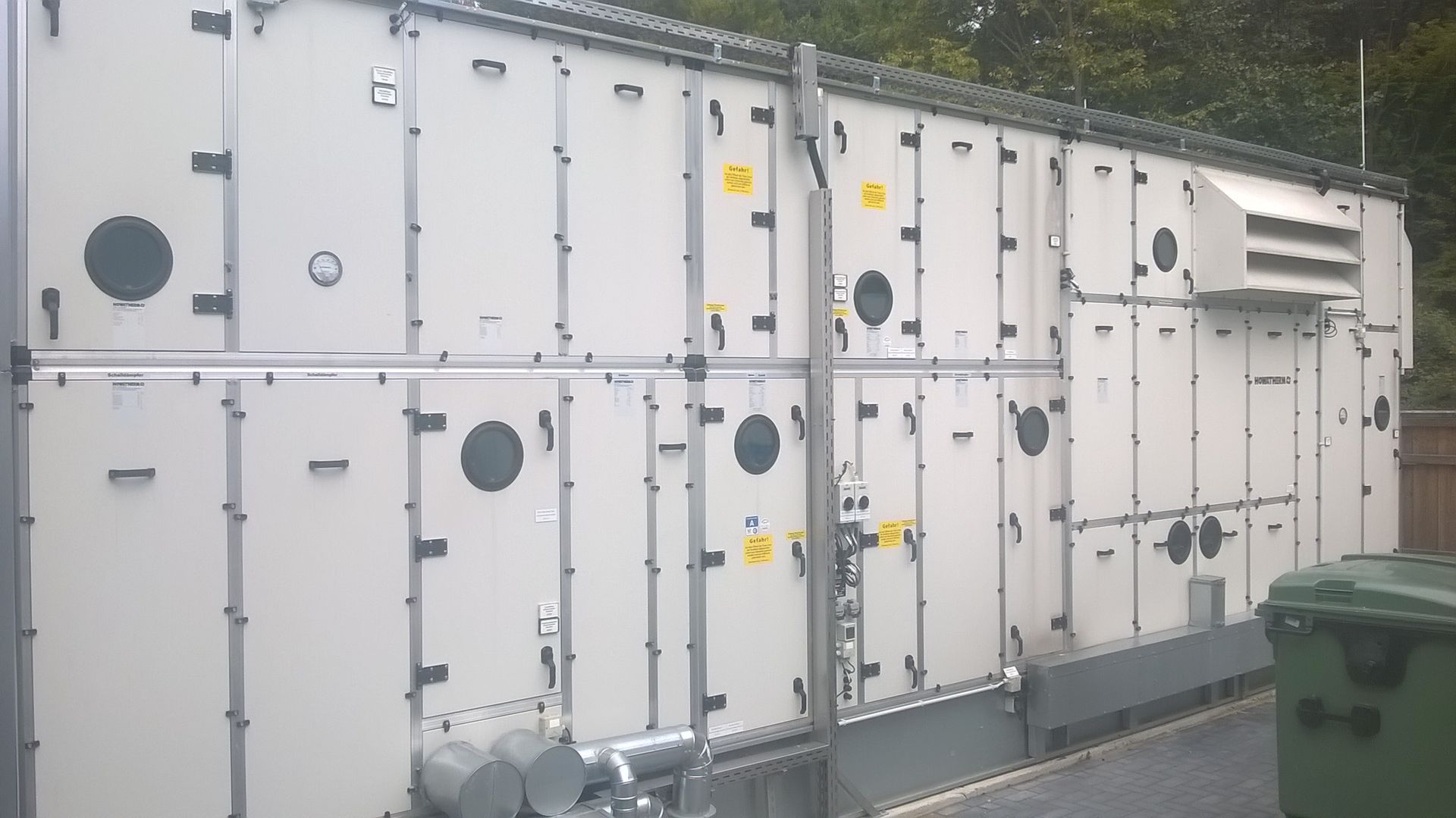 Große, industrielle Klimaanlage mit mehreren rechteckigen Paneelen, Zugangsöffnungen und Lüftungsöffnungen.