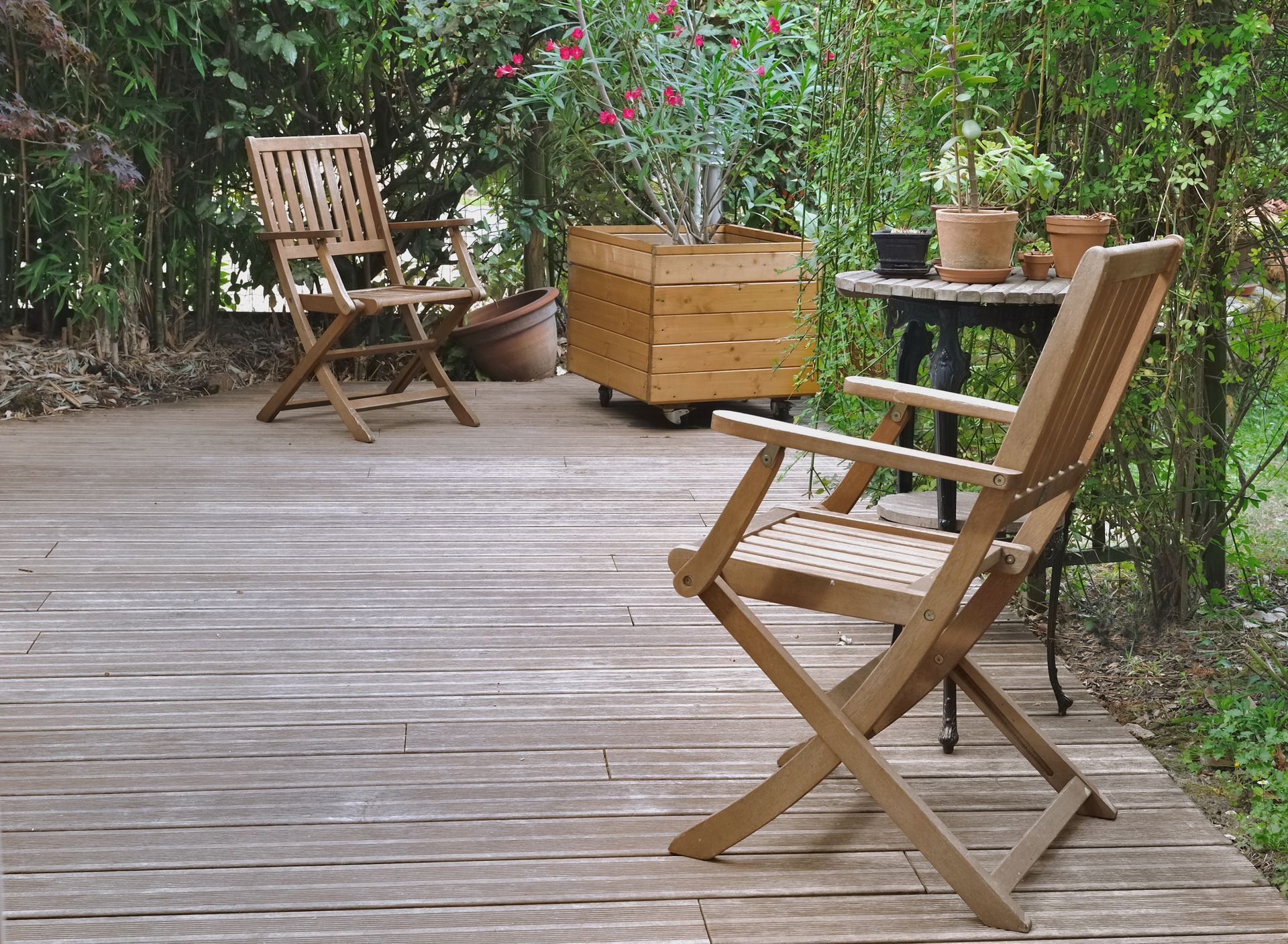 Terrasse en bois avec chaises pliantes, table et plantes en pot au milieu d'une végétation luxuriante.