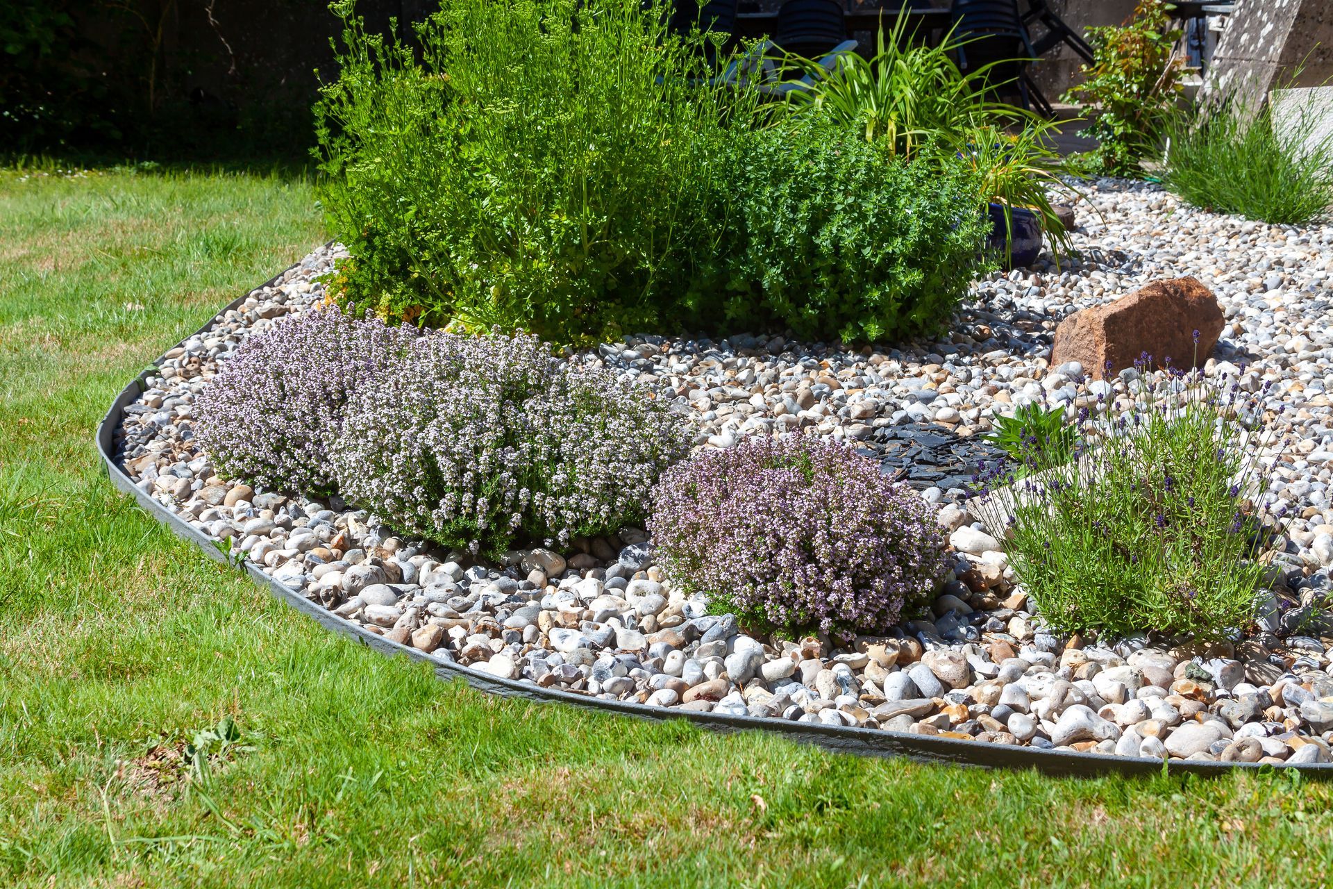 Massif de jardin incurvé bordé de pierres, agrémenté d'arbustes verts et de gravier blanc, jouxtant une pelouse.