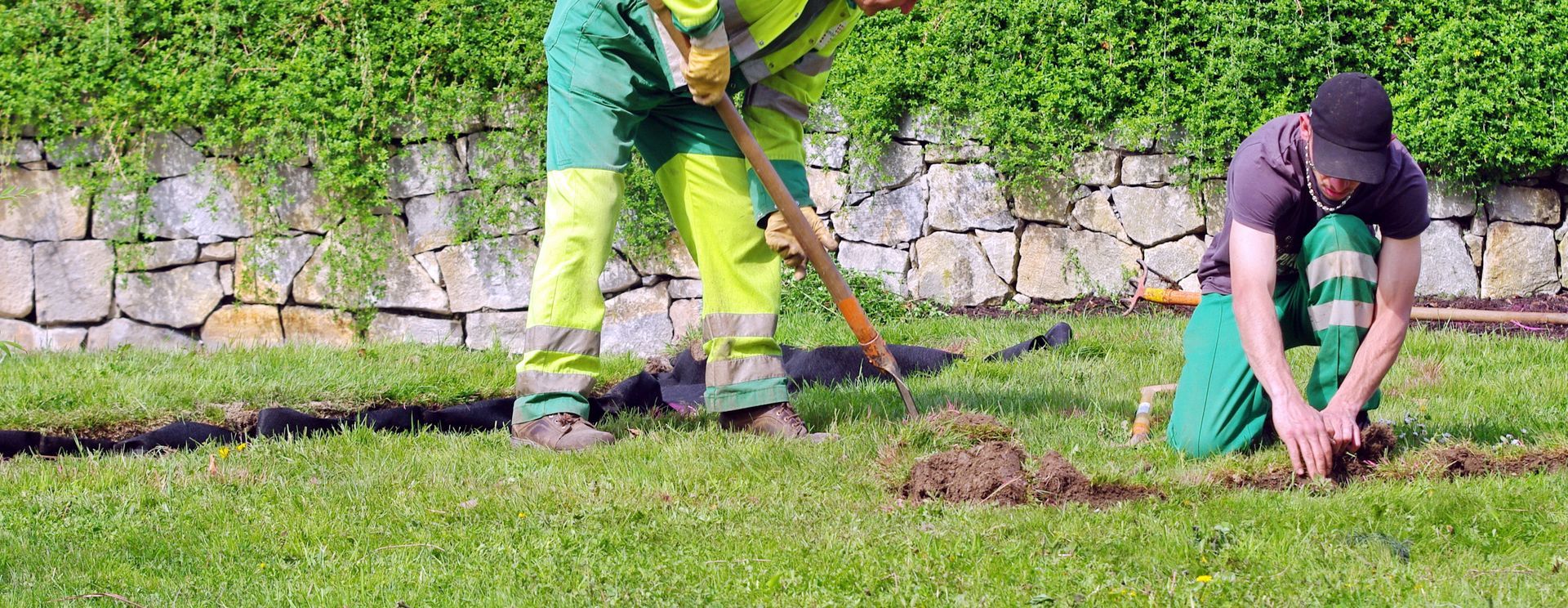 Deux personnes jardinent sur une pelouse, l'une creuse avec une pelle et l'autre s'agenouille pour planter des semis.