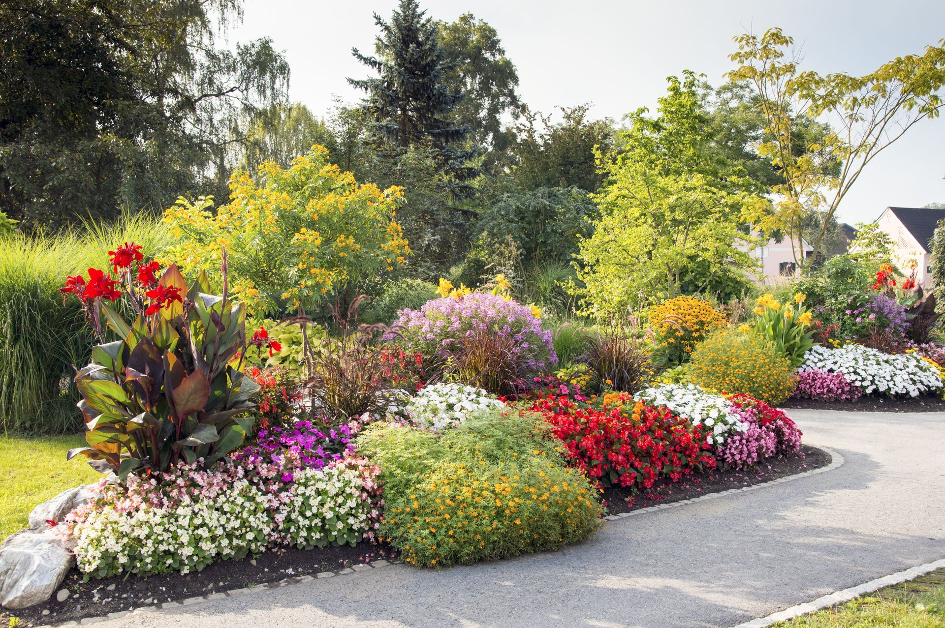 Des parterres de fleurs colorés bordent un chemin de jardin sinueux sous un soleil éclatant.