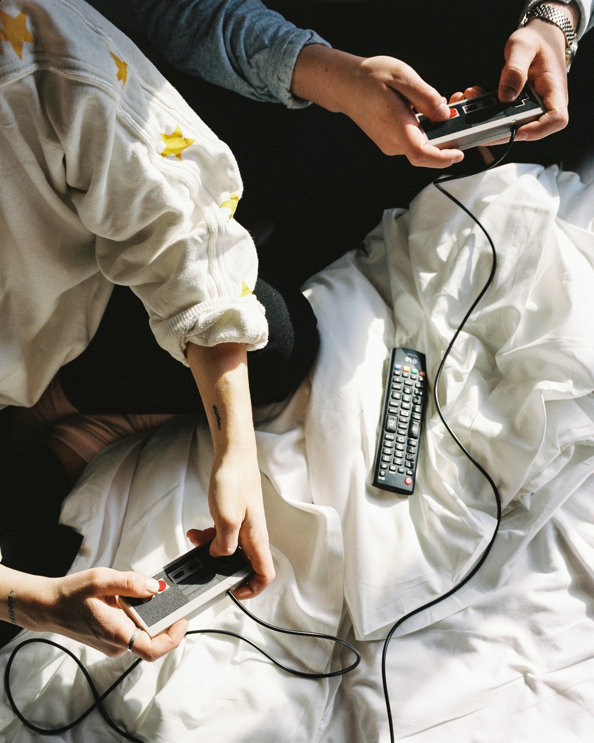 Zwei Personen sitzen in einem Bett mit Spielkonsolen in den Händen