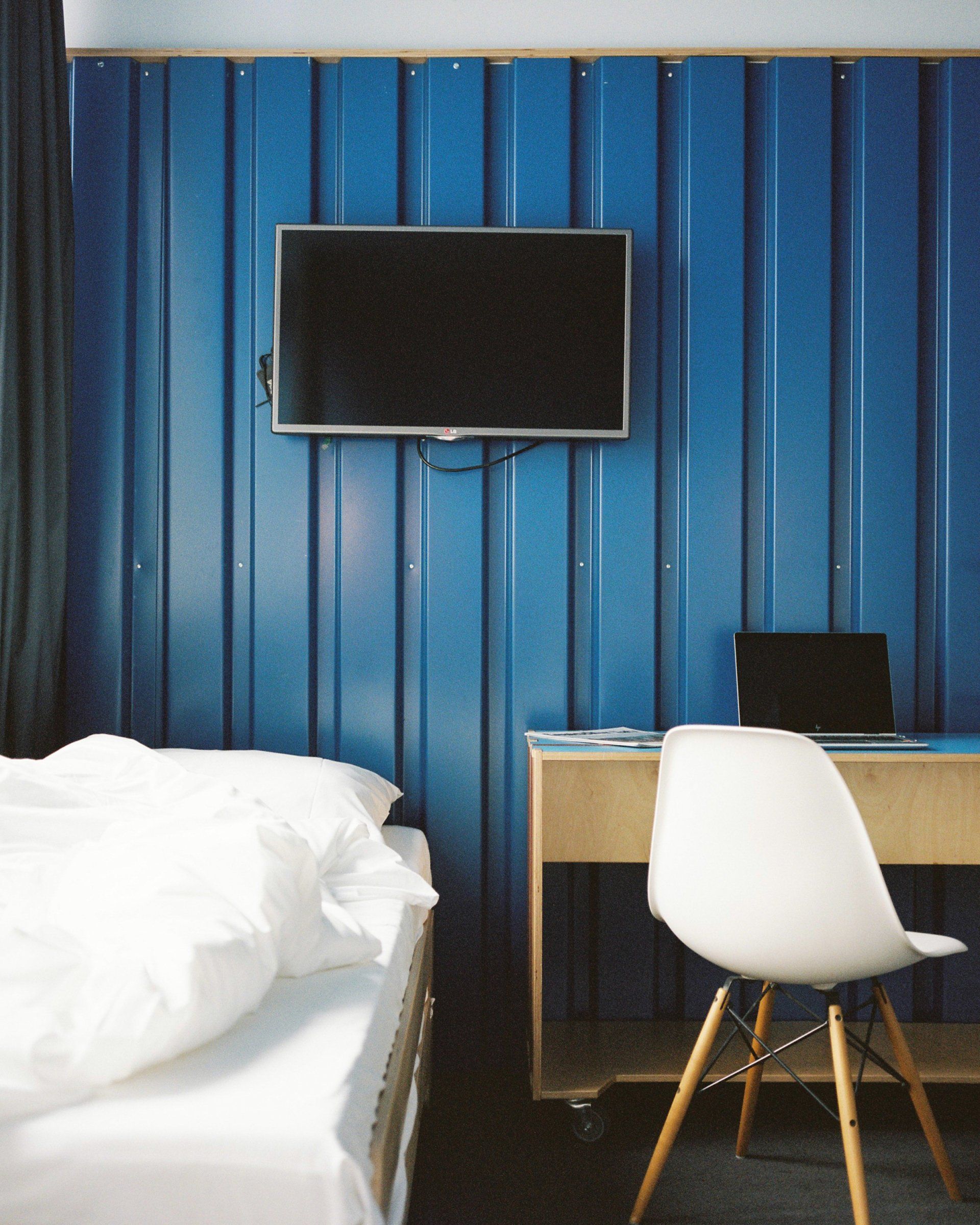 Weißer Stuhl vor Schreibtisch und TV, Bett teilweise sichtbar im Superbude-Zimmer