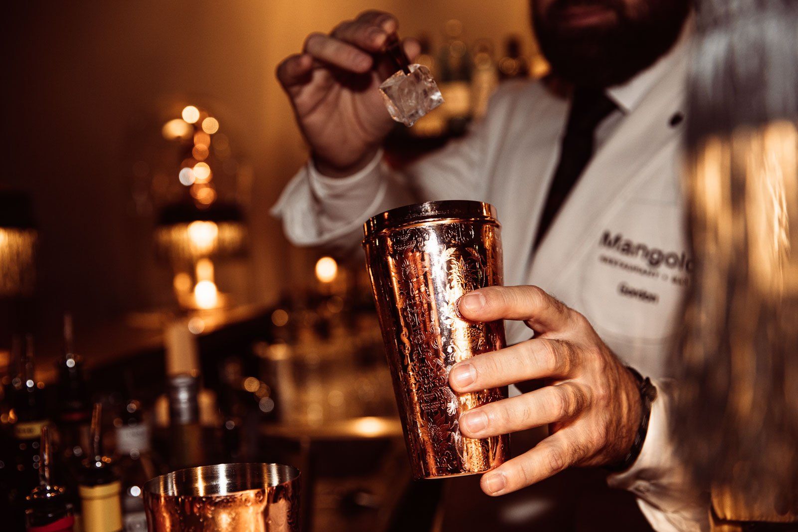 Barkeeper füllt Eiswürfel in einen Messing-Shaker in der Bar Mangold
