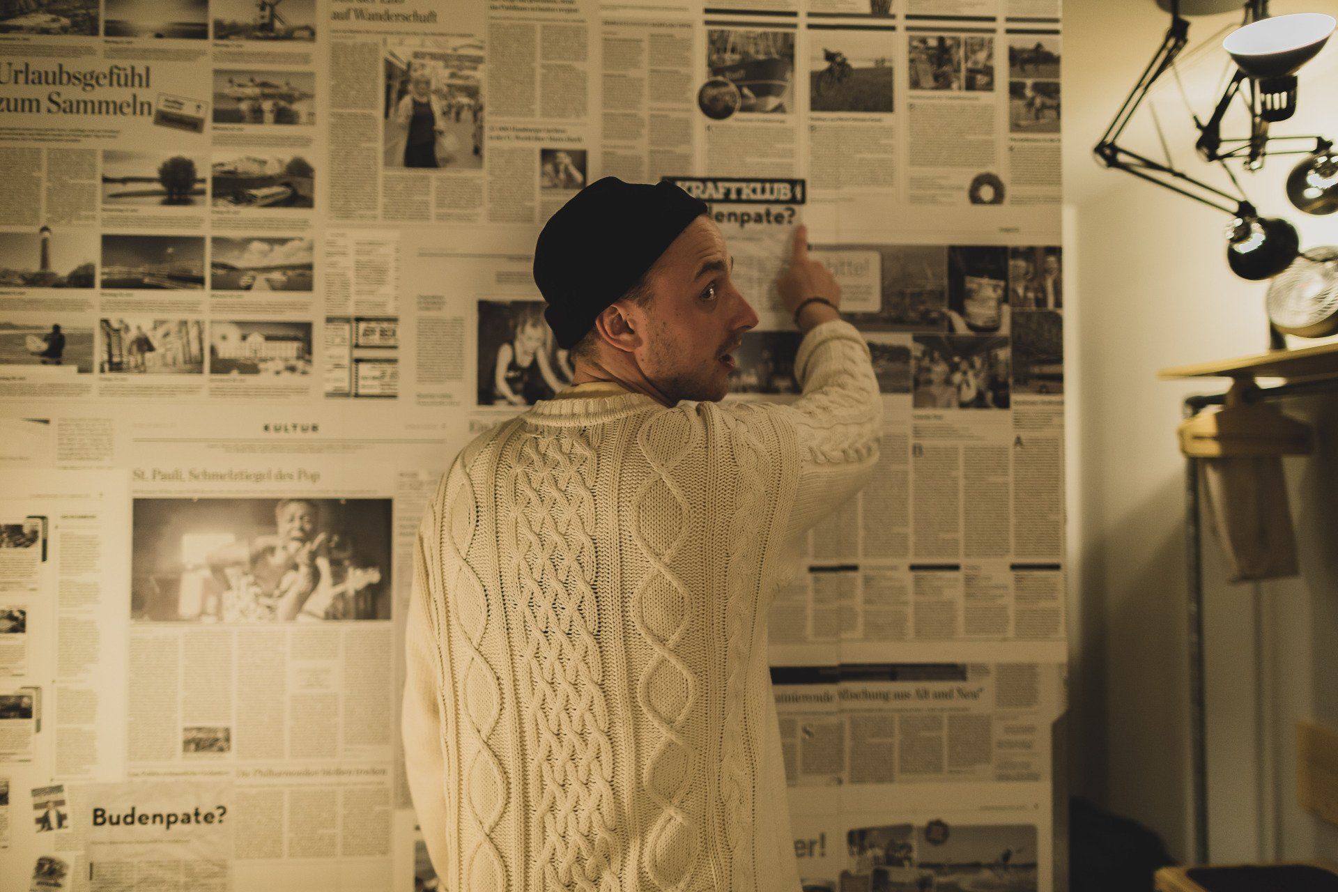 Männlich gelesene Person steht vor einer Wand mit Zeitungsausschnitten