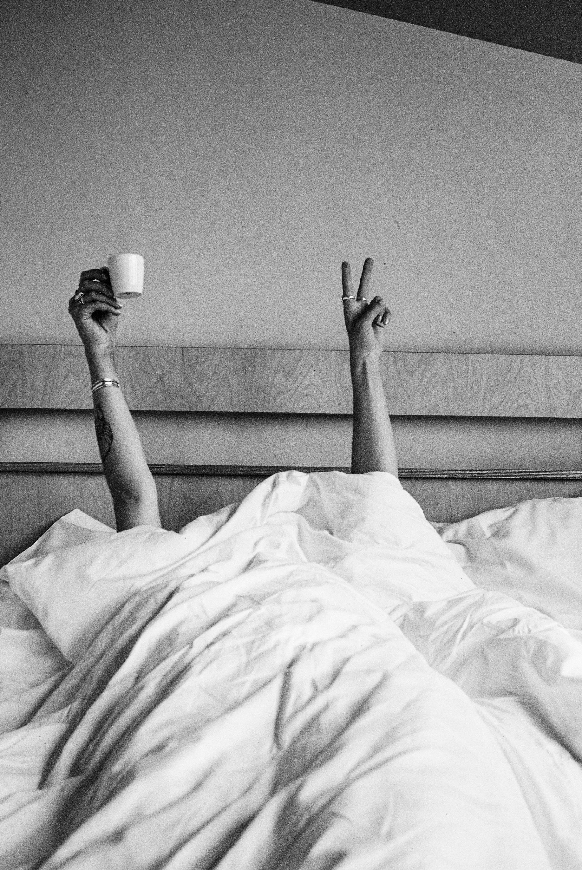 Person unter einer Bettdecke mit Kaffee in der Hand im Bett in einer Superbude