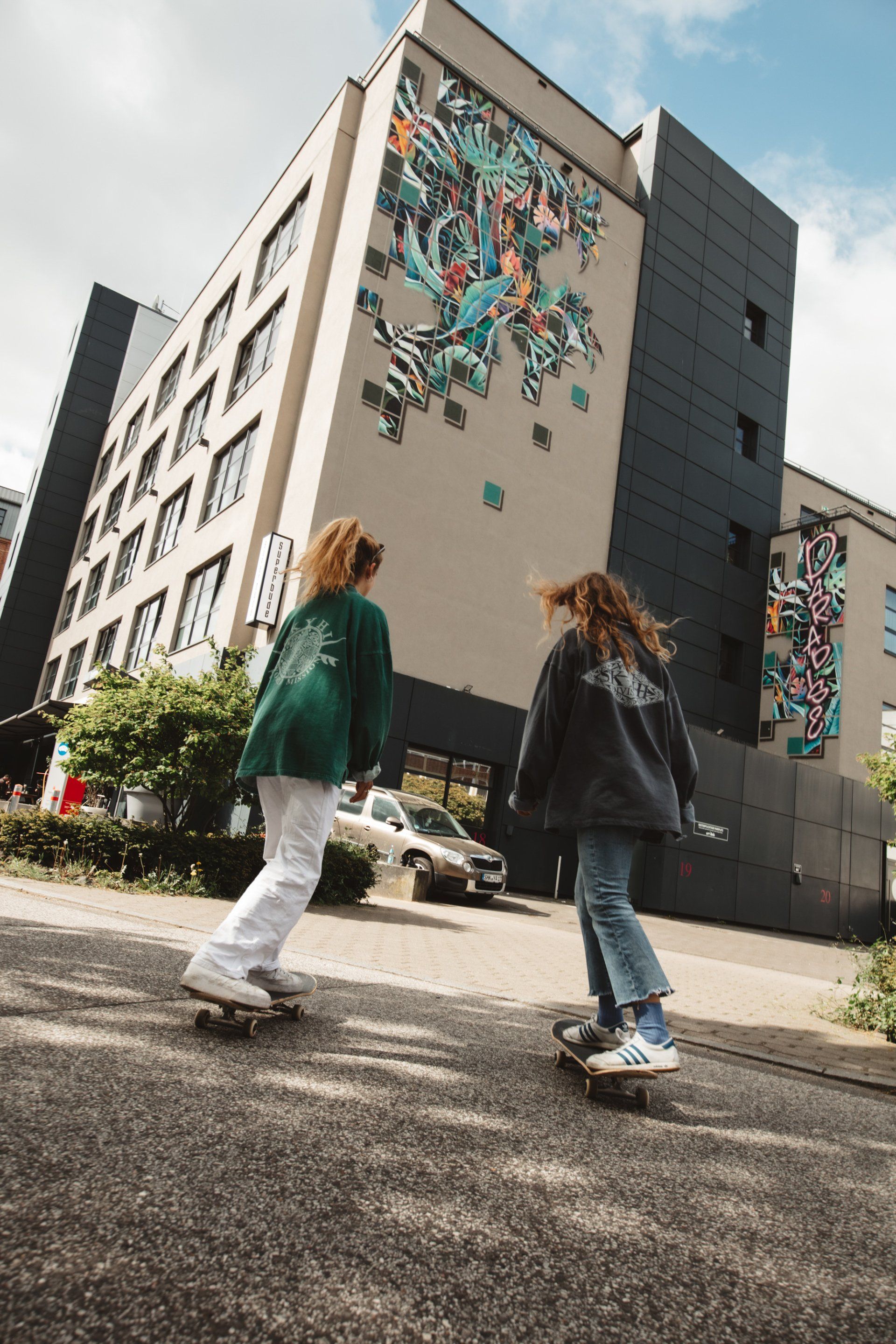 Zwei Personen auf Skateboards fahren auf die Superbude Altona zu
