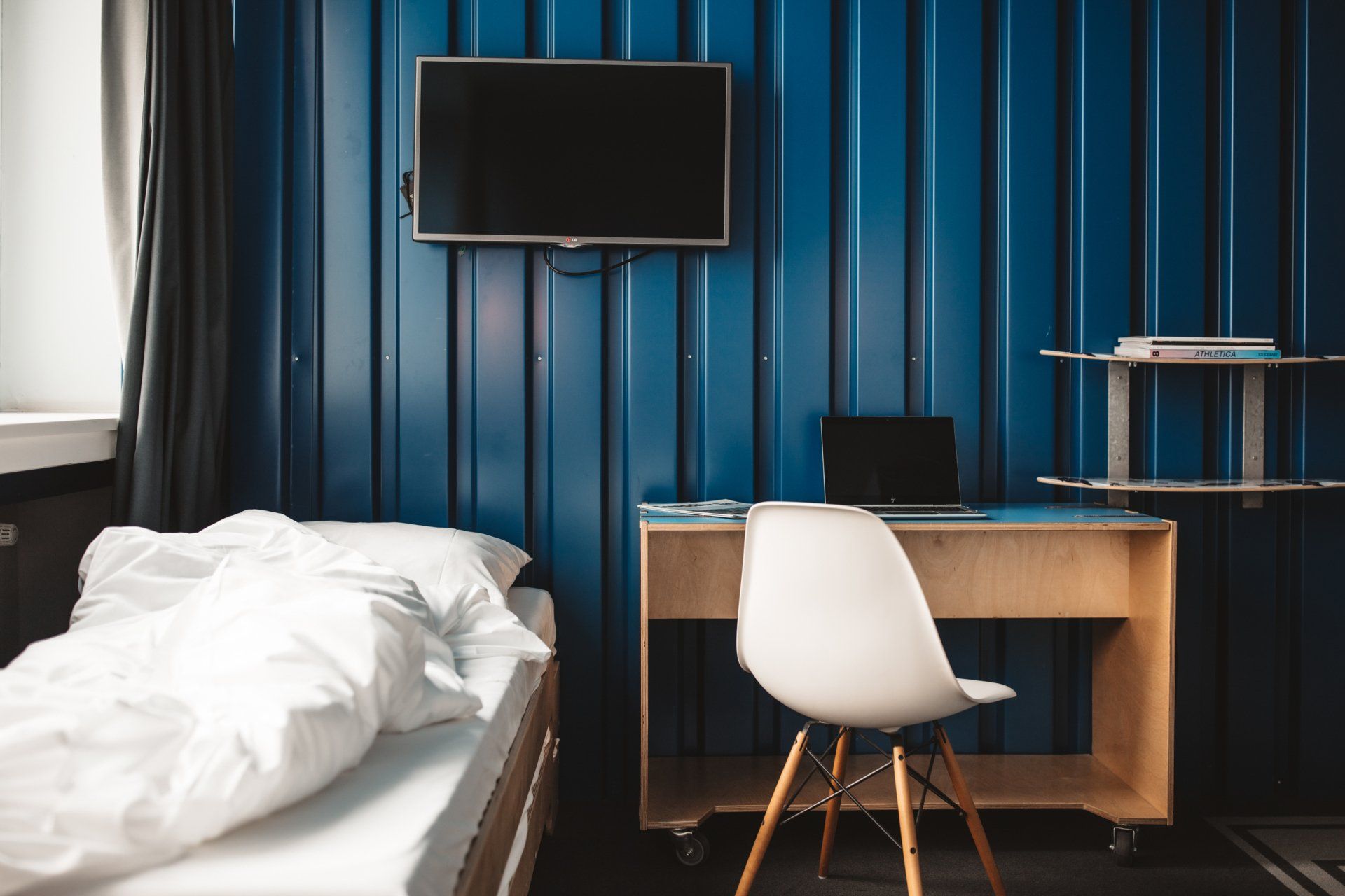 Zimmer in der Superbude mit weißem Stuhl, Schreibtisch, TV und teilweisem Bett