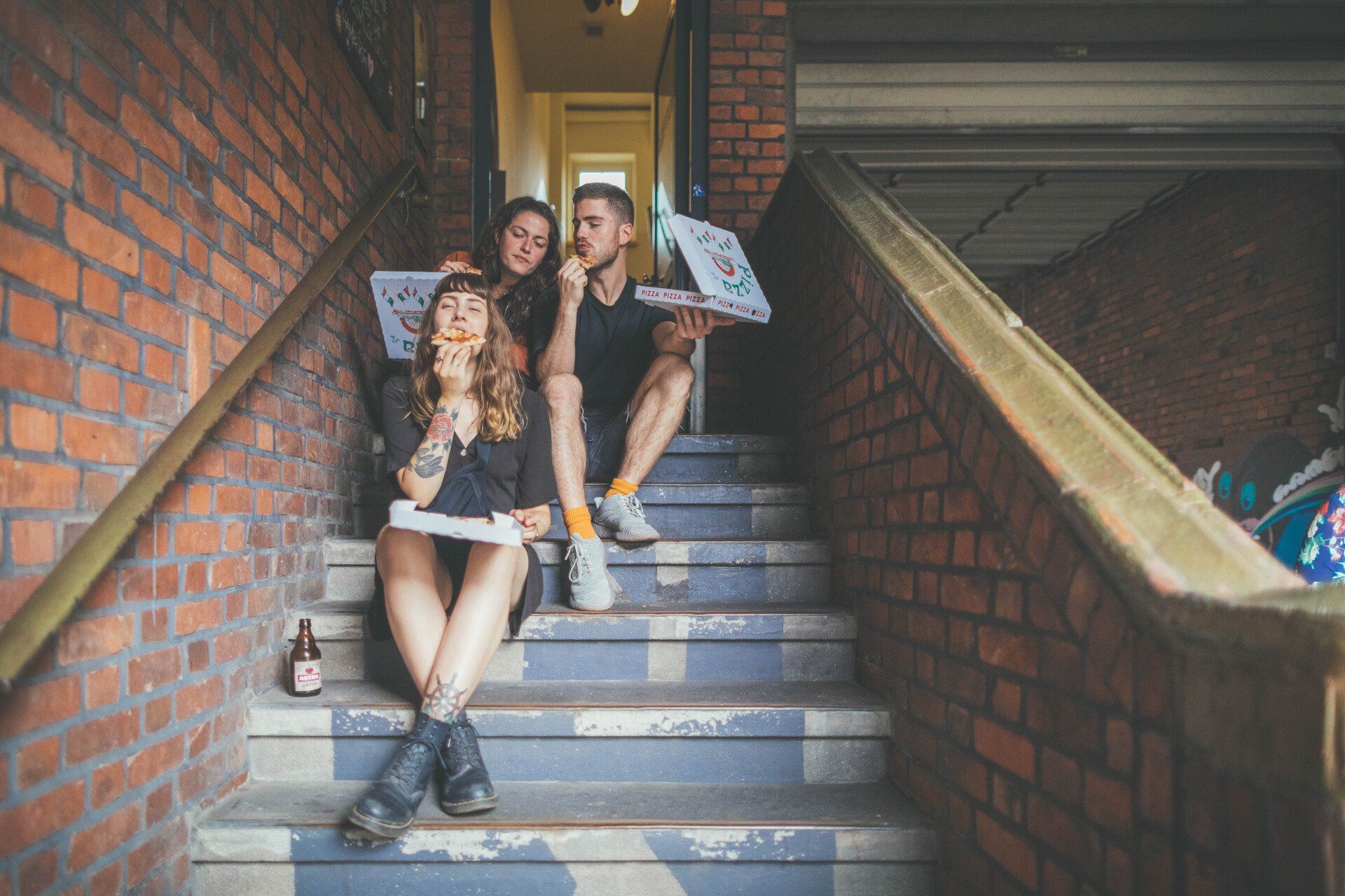 Drei Personen sitzen auf einer Treppe und essen Pizza aus Pizzakartons