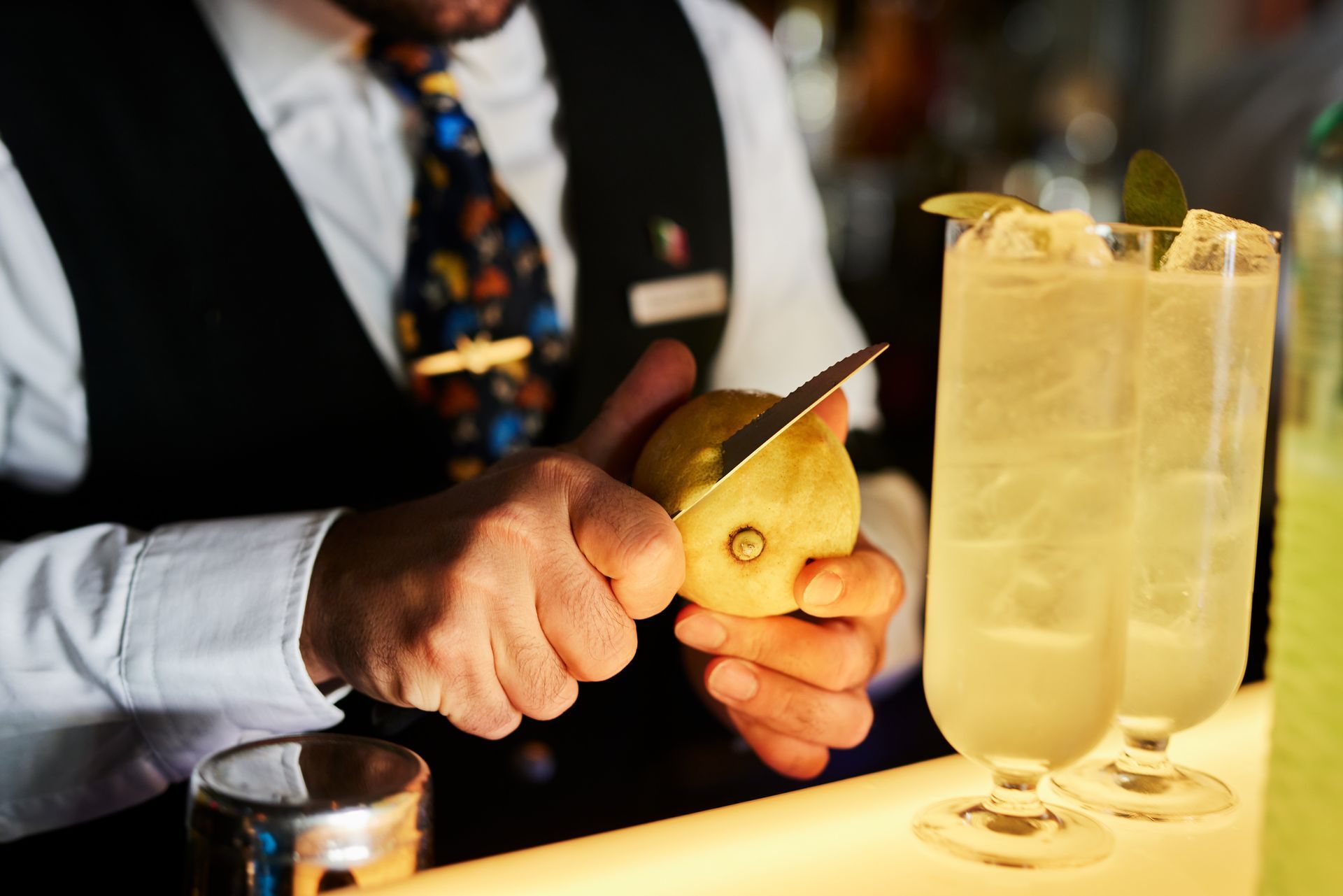 Barkeeper schält eine Zeste von einer Zitrone im Vordergrund Drinks