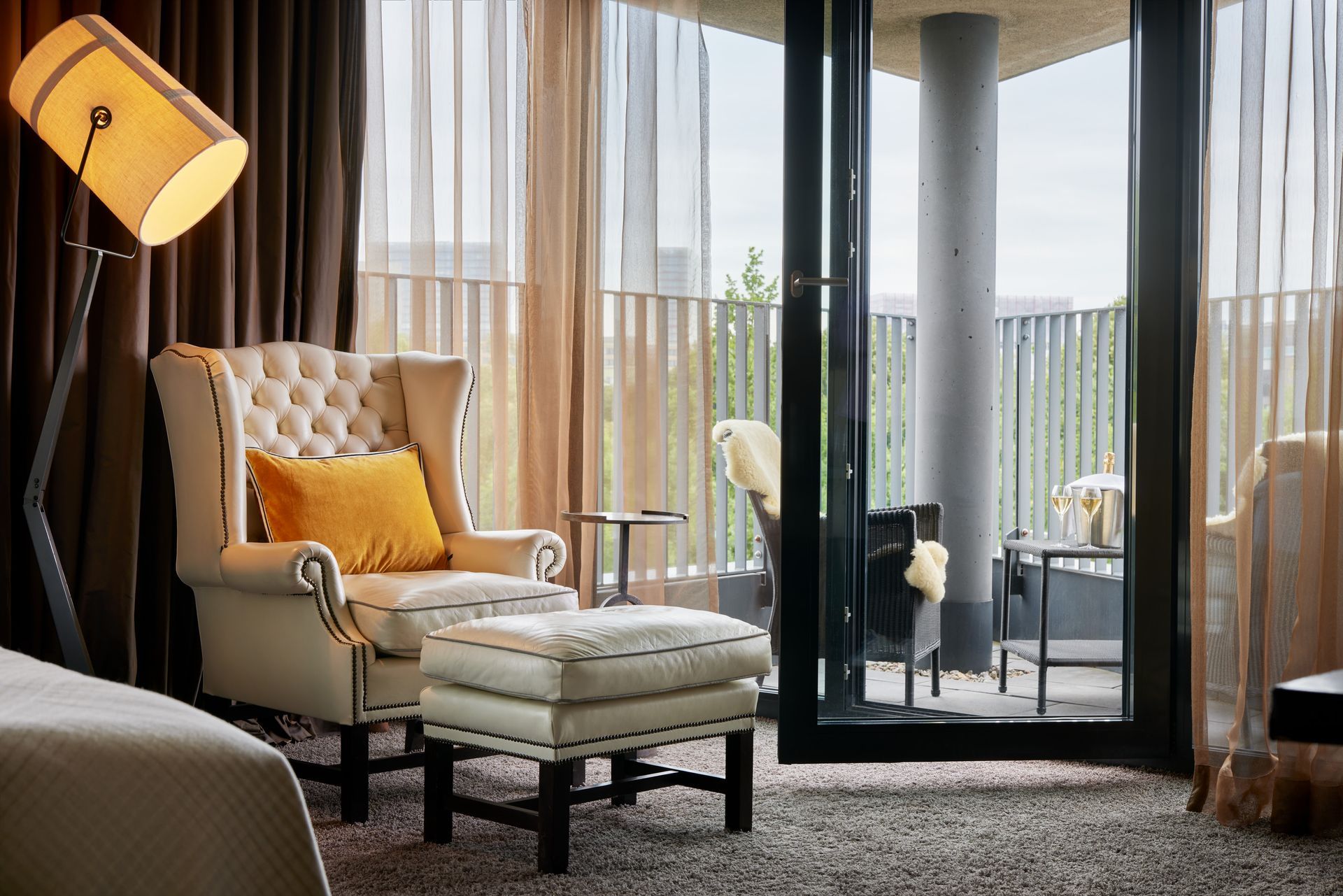 Weißer Chesterfield Sessel mit Fußhocker im Hintergrund ein Balkon in der Junior Suite