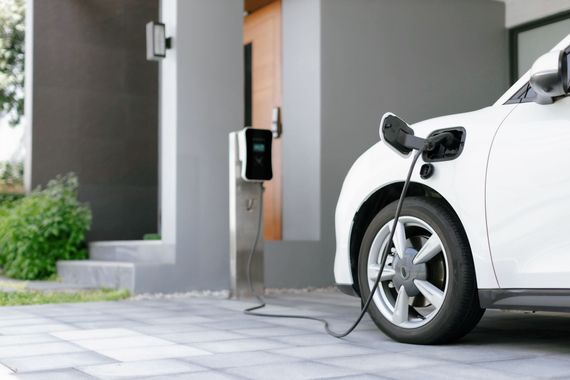 Voiture électrique en charge à une borne de recharge domestique à côté d'un garage.