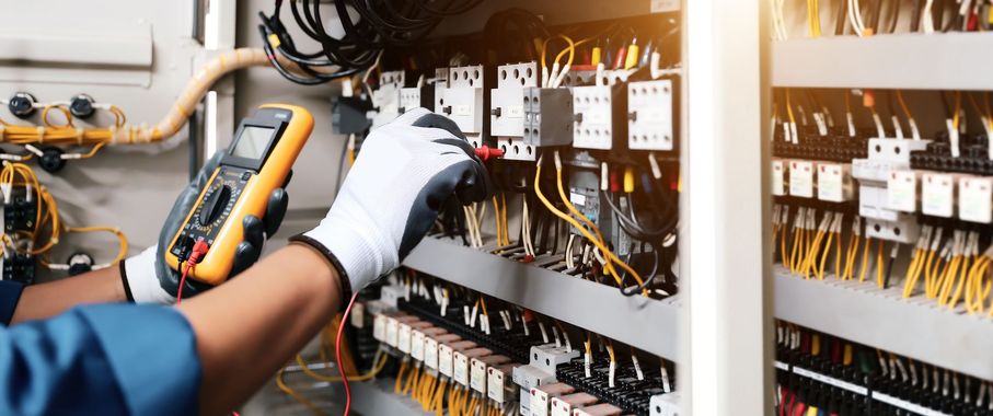 Un technicien teste le câblage d'un tableau électrique à l'aide d'un multimètre.