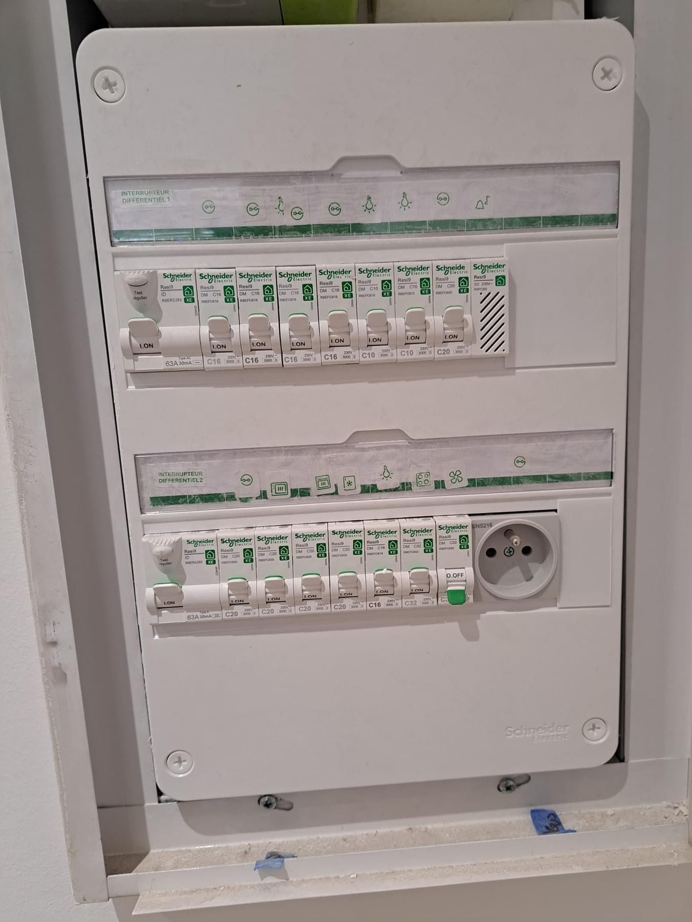 Tableau électrique encastré dans un mur, comportant deux rangées de disjoncteurs et une prise de courant.