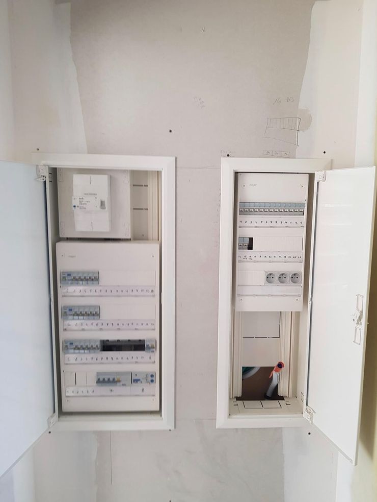 Panneaux électriques ouverts, encastrés dans un mur, avec portes et câblage apparent.