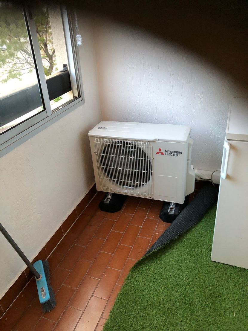 Un climatiseur portable dans une petite pièce près d'une fenêtre, à côté d'un gazon artificiel.