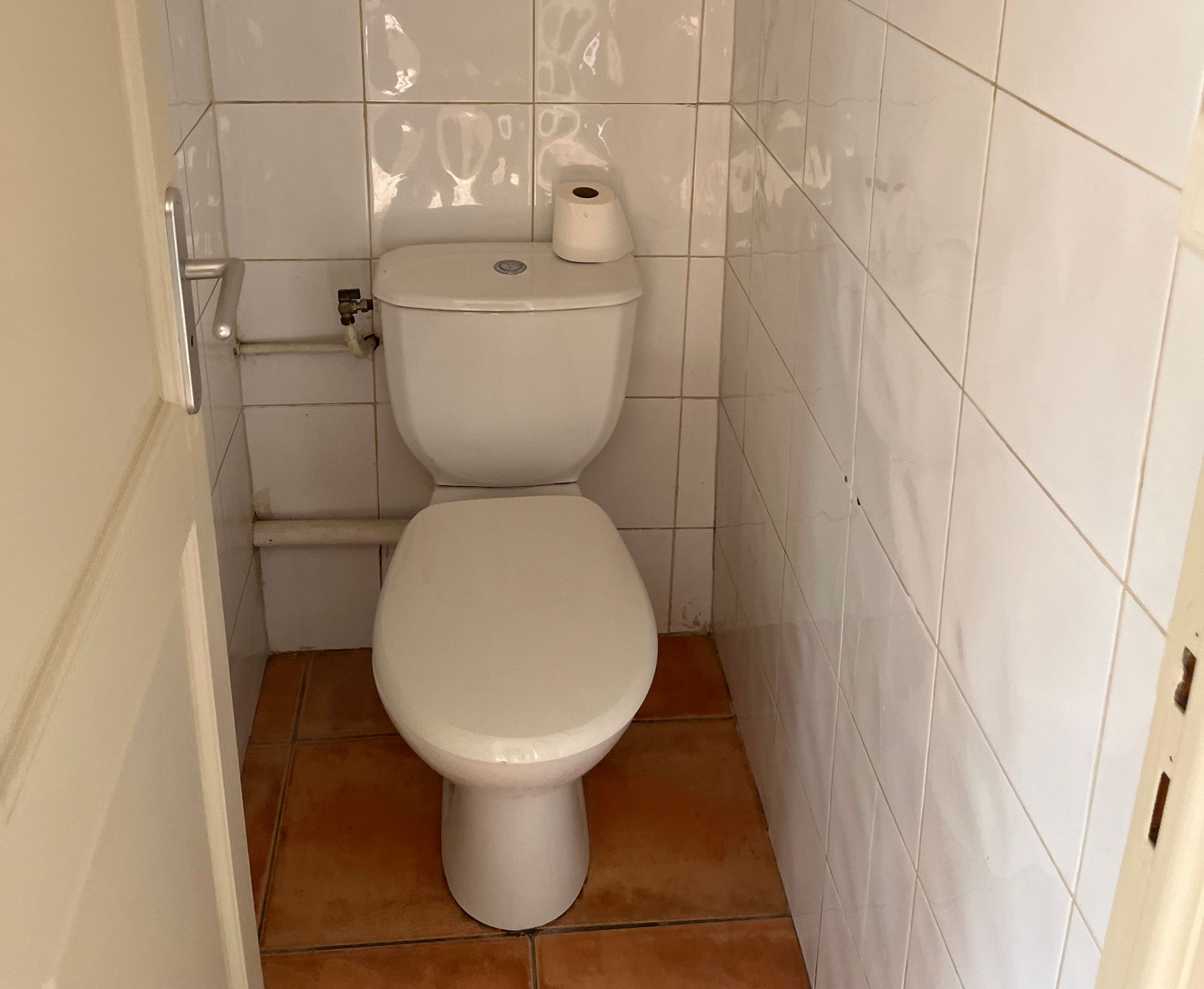 Salle de bains étroite avec toilettes, murs carrelés et sol en terre cuite.