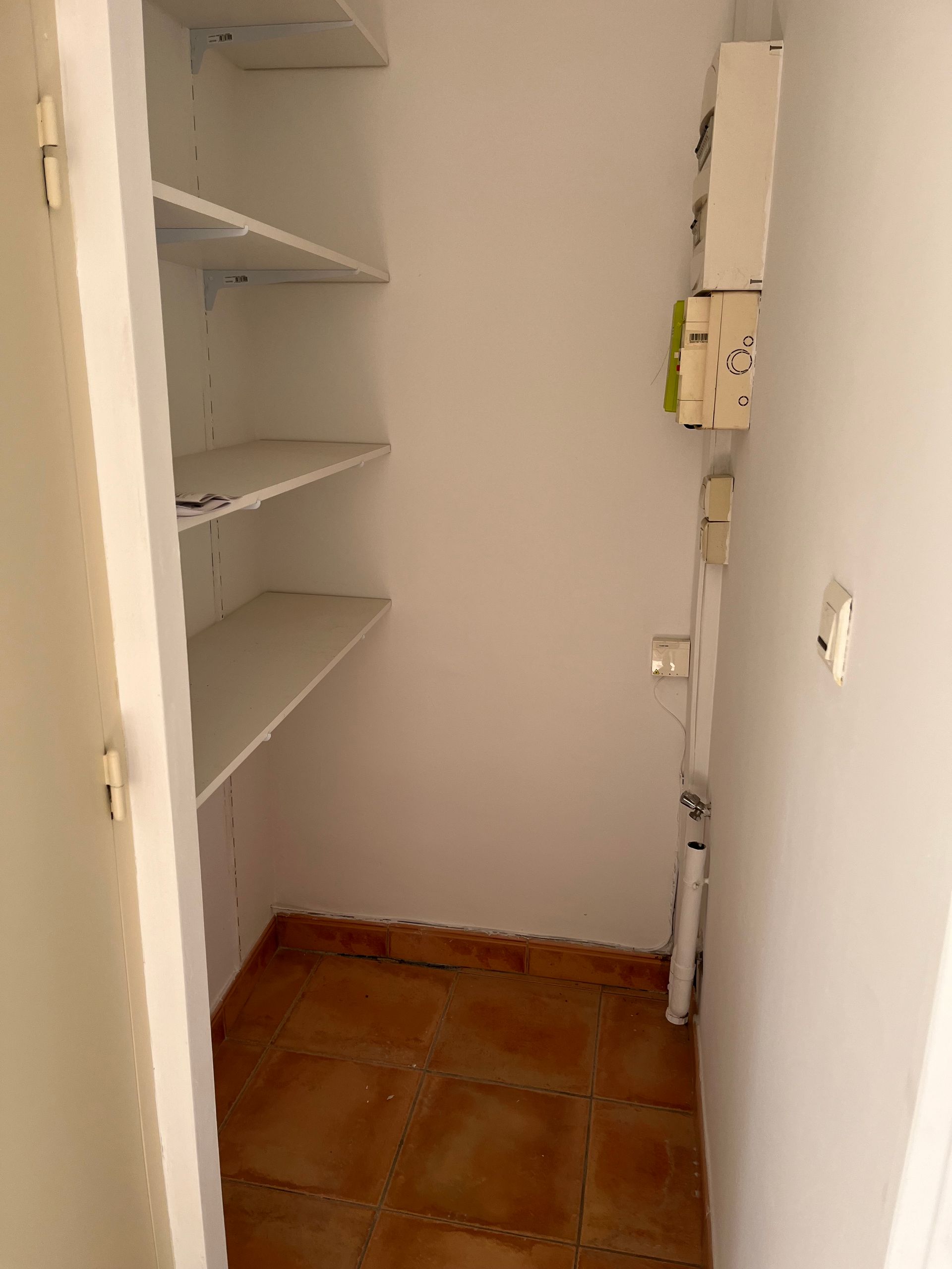 Placard garde-manger étroit avec étagères vides et sol en carrelage de terre cuite.