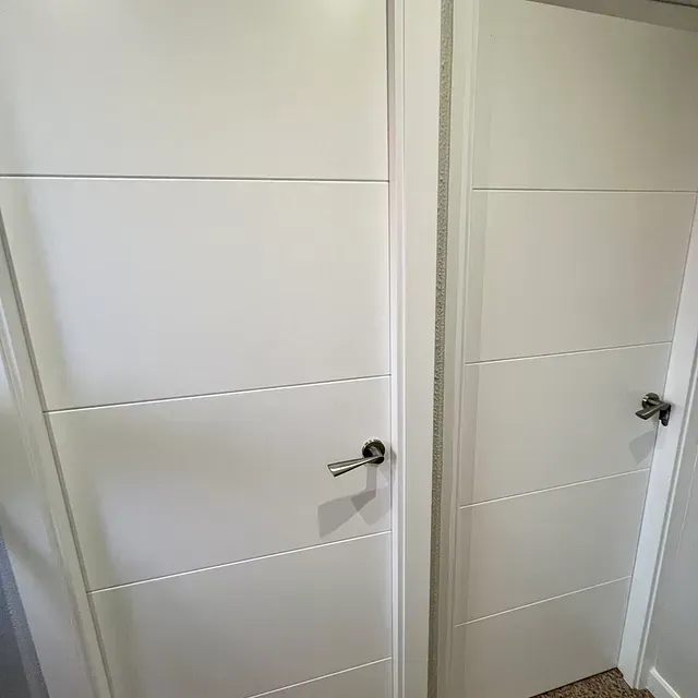 Un par de puertas blancas con tirador de acero inoxidable en un pasillo.