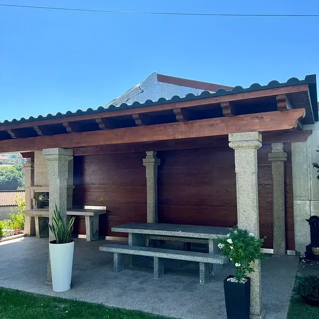 Un patio con mesa y bancos bajo un techo de madera.