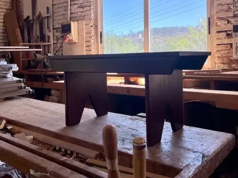 Un taburete de madera está sentado encima de una mesa de madera en un taller.