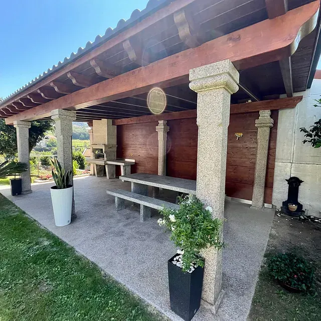 Un patio con mesa y bancos bajo un techo de madera.