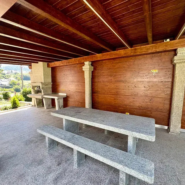 Una mesa de picnic con dos bancos bajo un techo de madera.