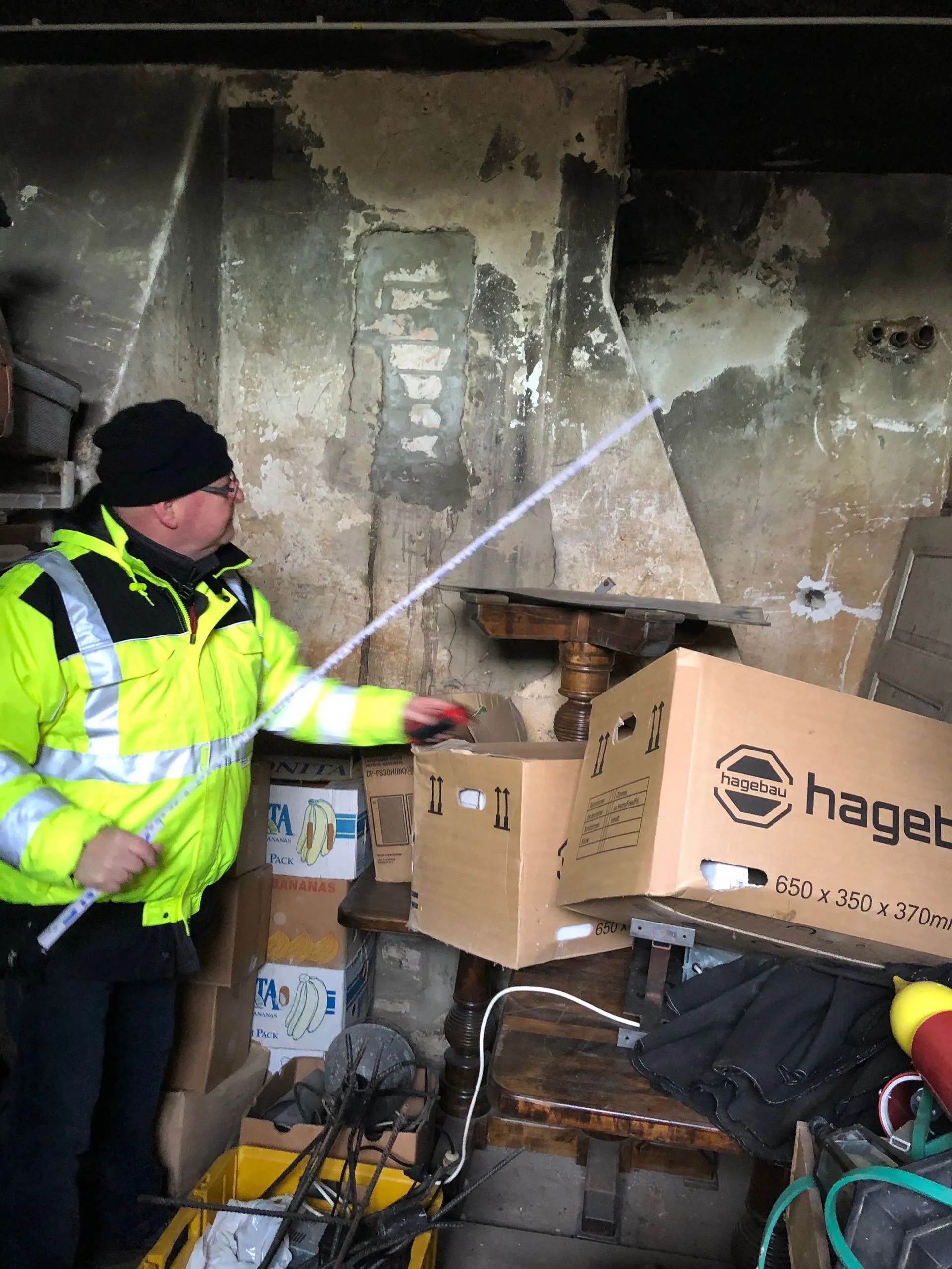 Ein Mann in einer gelben Jacke steht neben einem Karton mit der Aufschrift „Haget“.