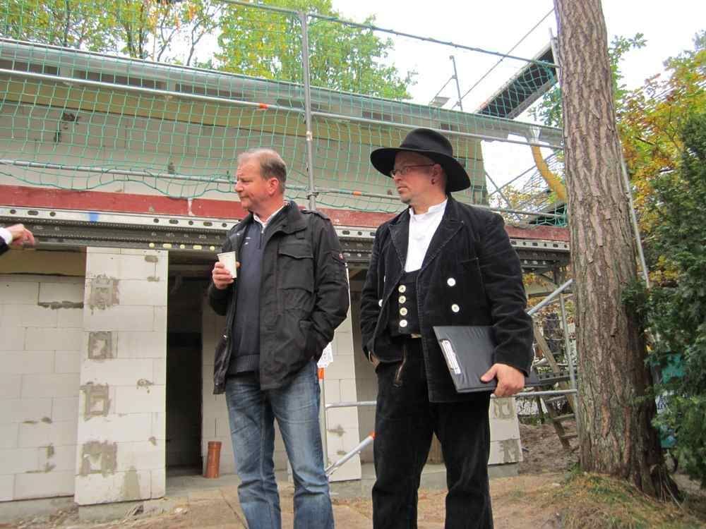 Zwei Männer stehen nebeneinander vor einem im Bau befindlichen Gebäude.