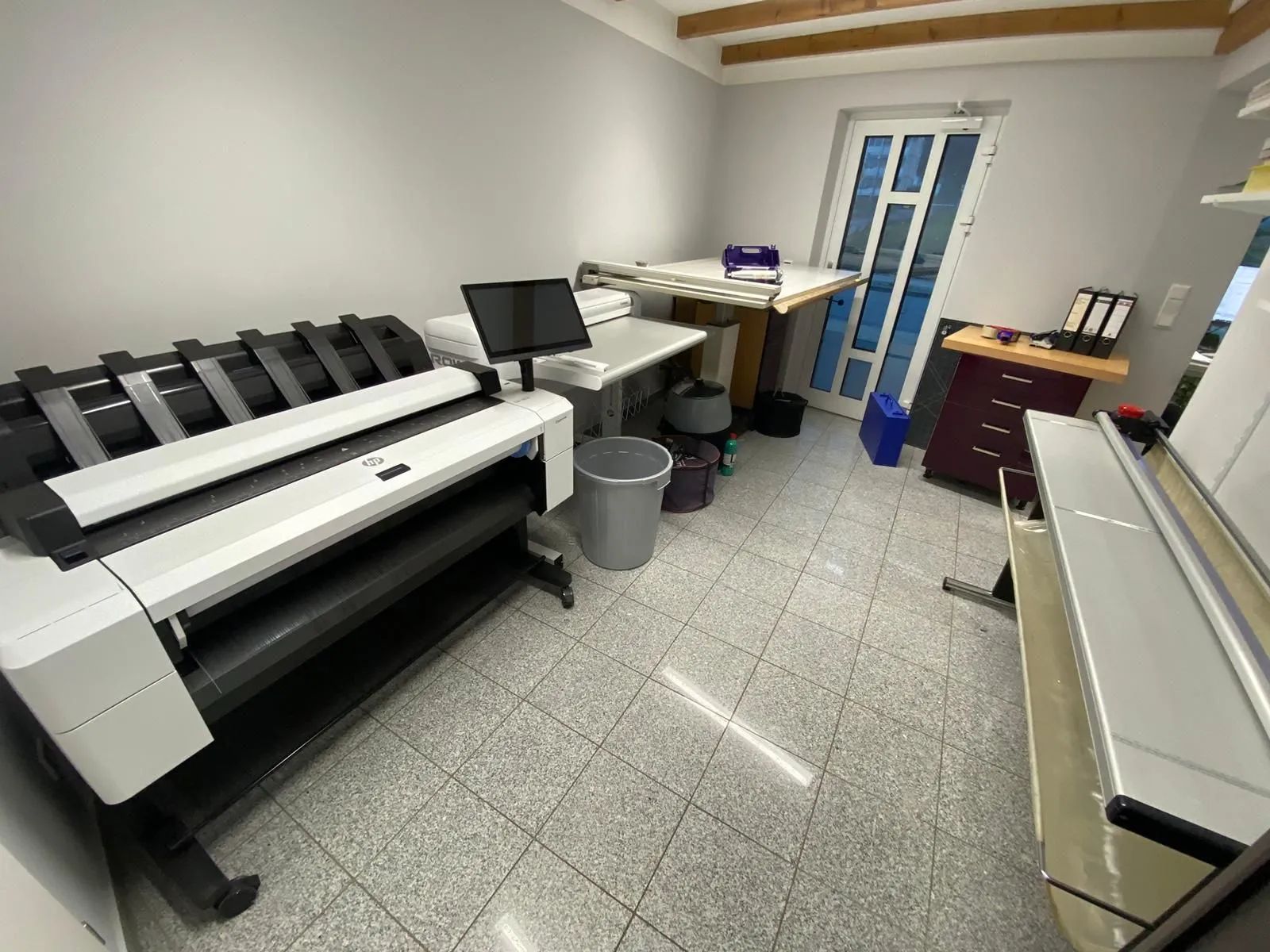 In einem Raum steht ein großer Drucker neben einem Schreibtisch.