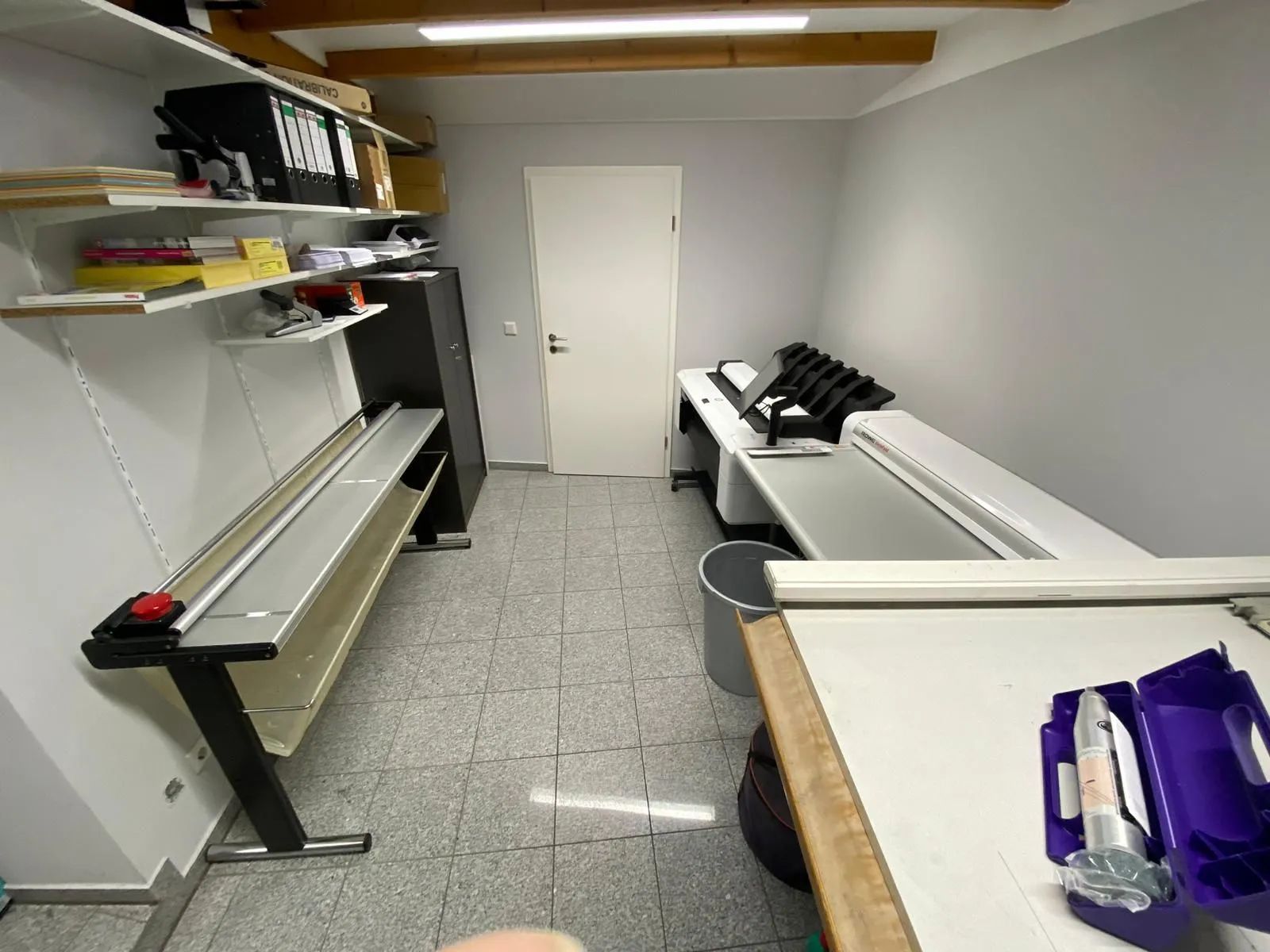 Ein Zimmer mit einem Schreibtisch, Regalen und einer Tür.