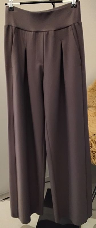 Graue Hose mit weitem Bein, die auf einem Kleiderbügel hängt, mit Bügelfalten vorne und Taschen.