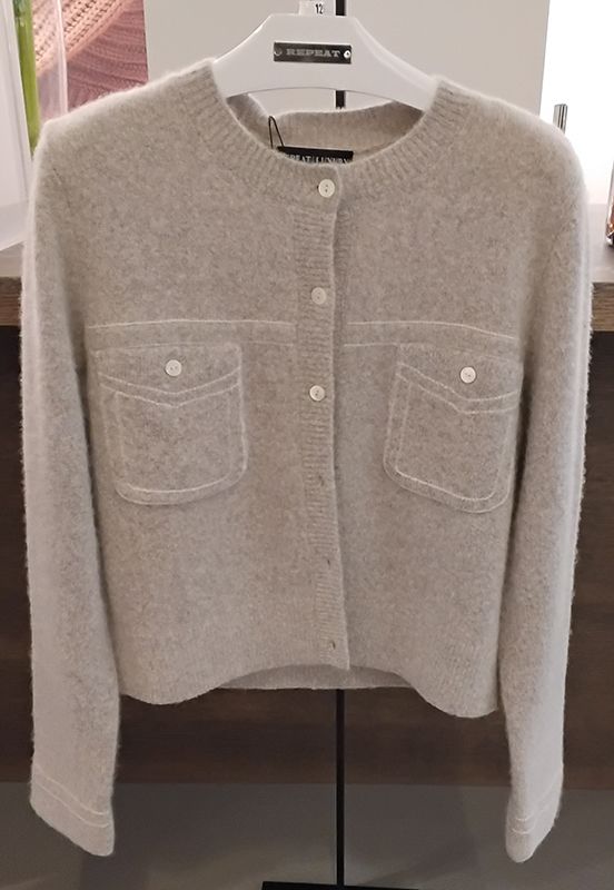 Beiger Strickjackenpullover mit Taschen und Knöpfen, hängt auf einem weißen Kleiderbügel.