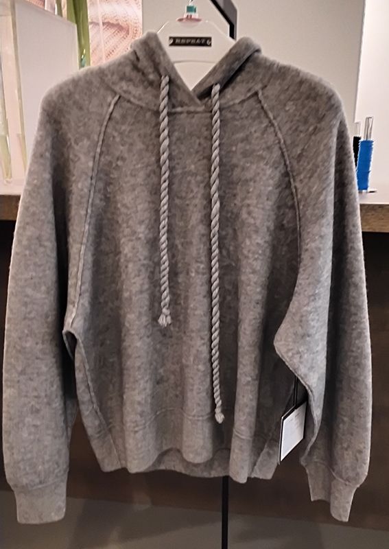 Grauer Kapuzenpullover mit Kordelzug, drinnen hängend.