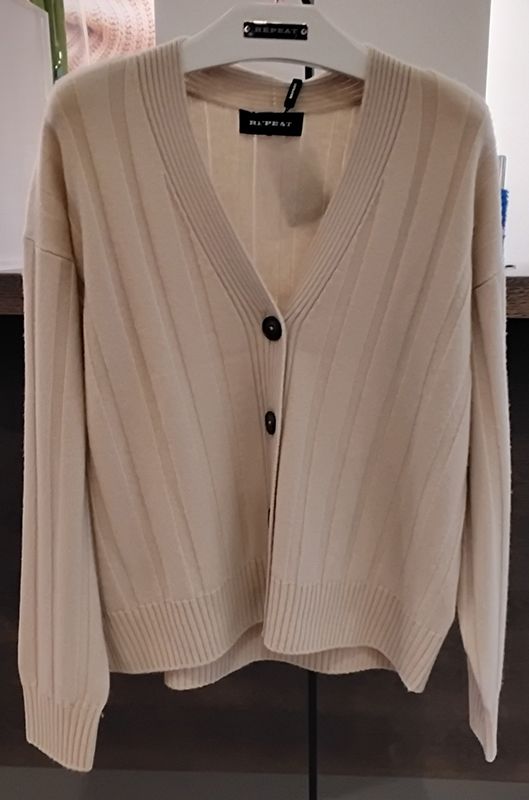 Beigefarbene Strickjacke mit V-Ausschnitt und Knopfverschluss hängt an einem Kleiderständer.