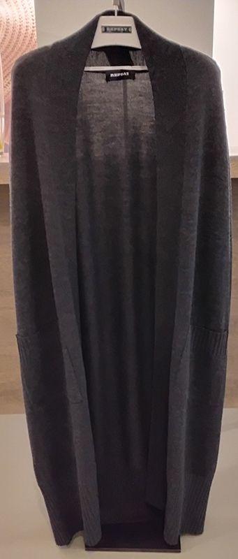 Eine lange, dunkelgraue Strickjacke hängt an einem weißen Kleiderbügel.