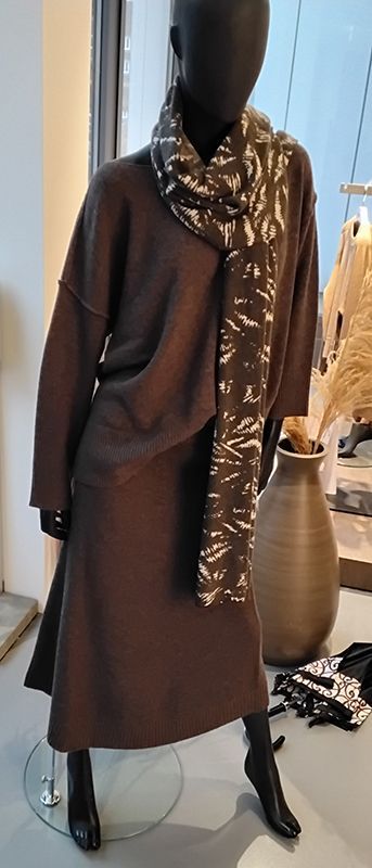 Eine Schaufensterpuppe mit braunem Pullover, Rock, Schal und Stiefeln in einem Laden.