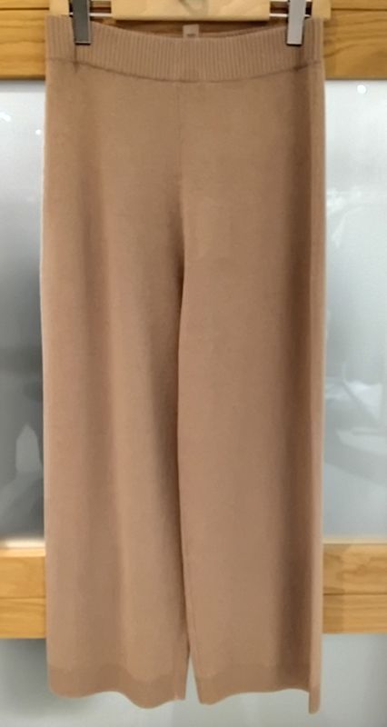 Hellbraune Strickhosen mit weitem Bein hängen auf einem Kleiderbügel vor einem Holzrahmen.