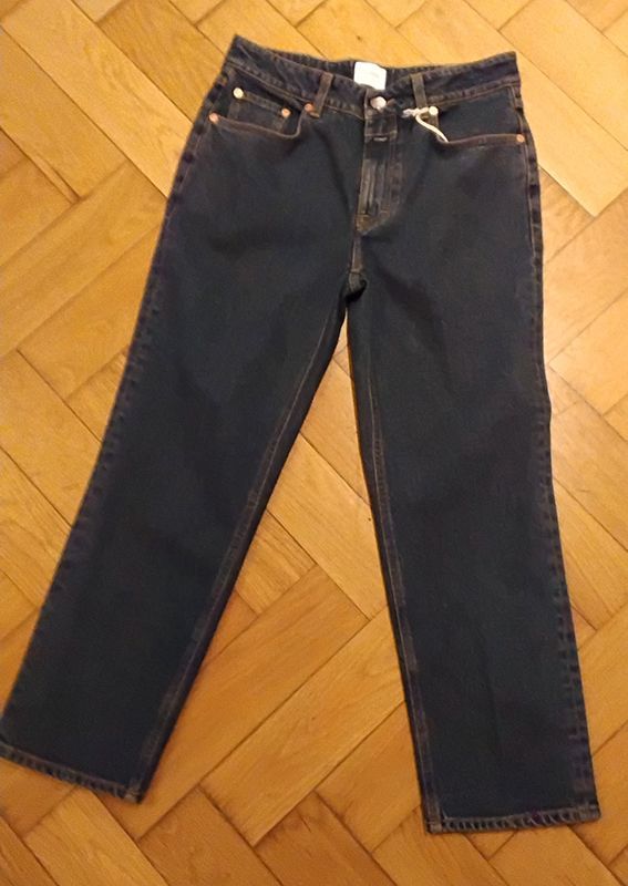 Dunkelblaue Jeans mit orangefarbenen Nähten, auf einem Holzboden liegend.