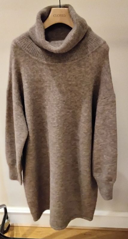 Übergroßer hellbrauner Strickpullover mit Wasserfallausschnitt, der auf einem hölzernen Kleiderbügel hängt.