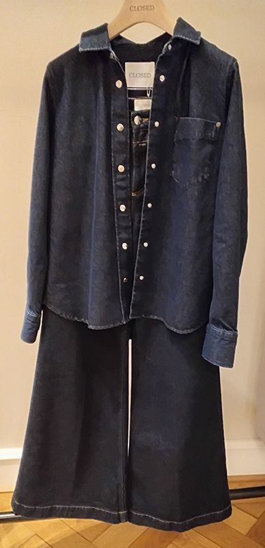 Dunkles Jeanshemd und Hose mit weitem Bein hängen auf einem hölzernen Kleiderbügel.