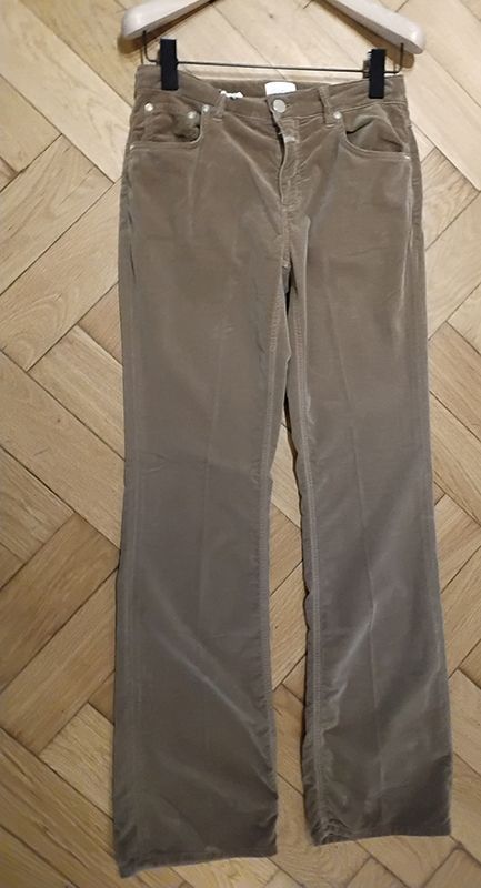 Braune Cordhosen hängen auf einem hölzernen Kleiderbügel vor einem Hintergrund aus Holzpaneelen.