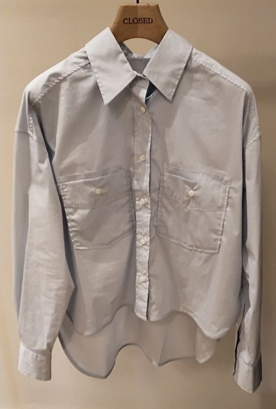 Hellblau-weiß gestreiftes Button-Down-Hemd mit zwei Vordertaschen, hängt auf einem Holzbügel.