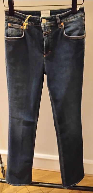 Dunkelblaue Jeans aus Denim, die auf einem Kleiderbügel hängen, mit weißem Besatz an den Taschen.