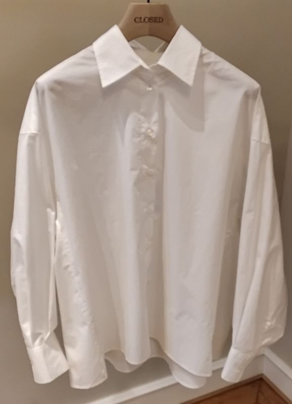 Weißes Button-Down-Hemd mit Kragen, das auf einem hölzernen Kleiderbügel mit der Aufschrift „GESCHLOSSEN“ hängt.