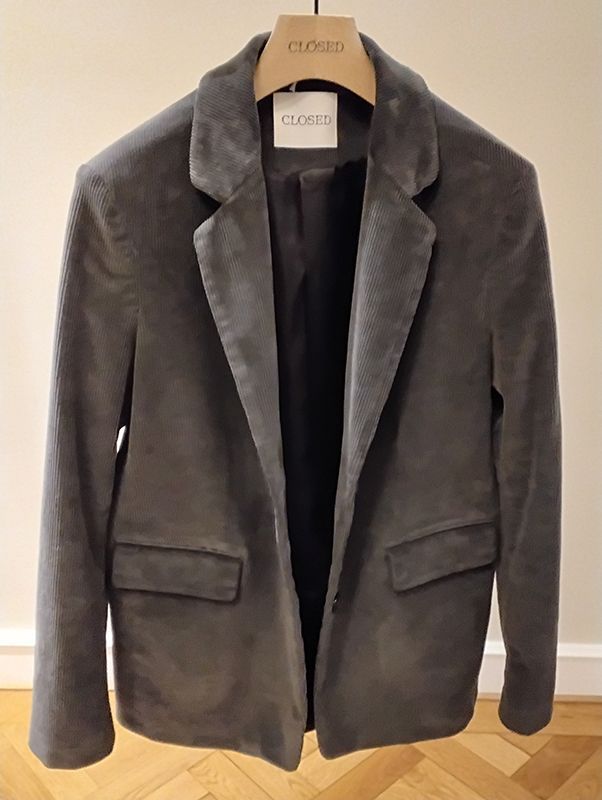 Grauer Cordblazer hängt an einem hölzernen Kleiderbügel.