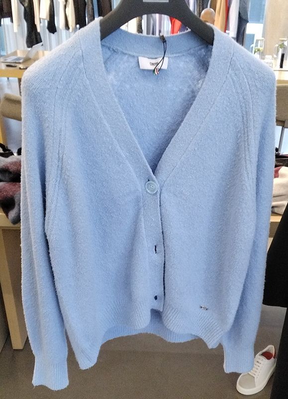 Hellblauer Cardigan-Pullover mit V-Ausschnitt und Knopfverschluss, hängt an einer Stange.